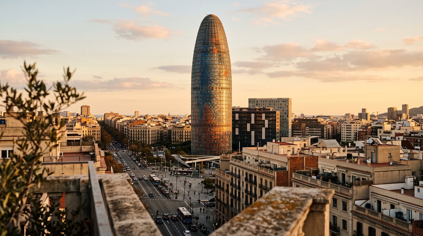 Torre Glòries at golden hour, its shimmering façade rising above Poblenou with the city grid stretching out below